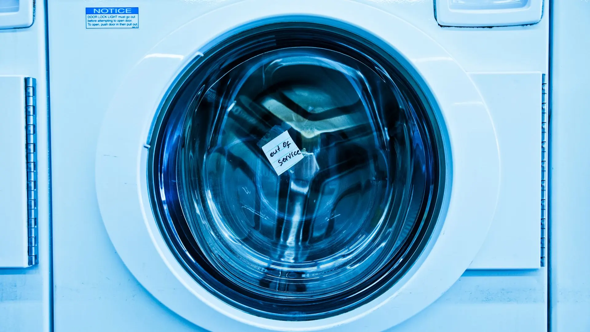 Close-up of an out-of-service washing machine in a laundromat with a blue tint.