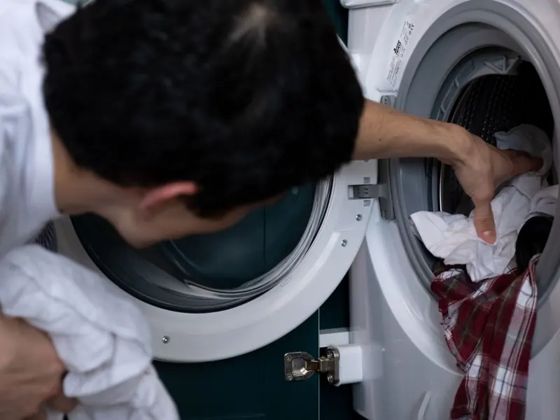 Close-up of a man placing clothes into a washing machine during household chores.