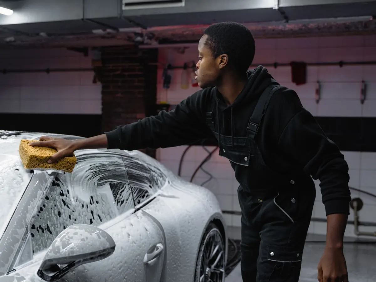A person washing a car with a sponge, deep cleaning in a garage setting.