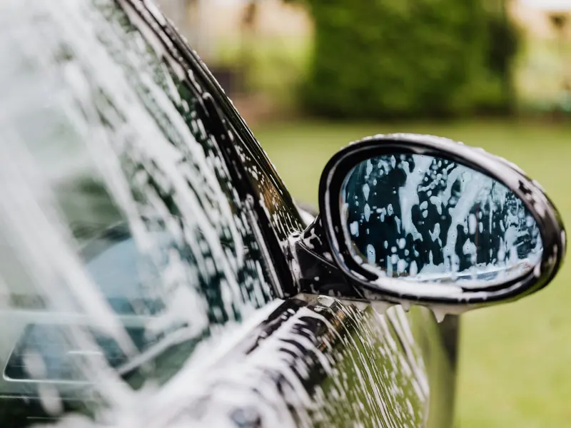 A detailed view of a car side mirror with soap suds, highlighting car wash detail.