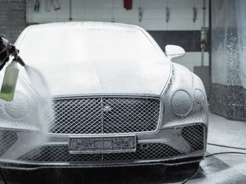 A luxury car is covered in foam during a detailed wash inside a garage.