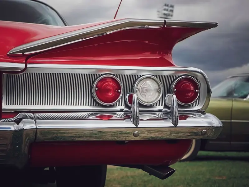 Close-up of a vintage red car tailfin and lights, showcasing retro chrome details.