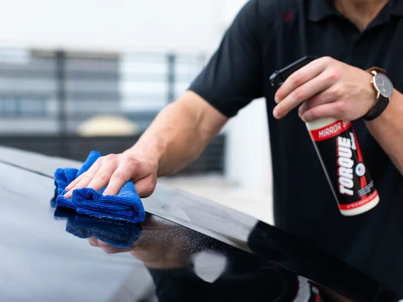 Hands cleaning car with microfiber cloth and spray cleaner for a shiny finish.