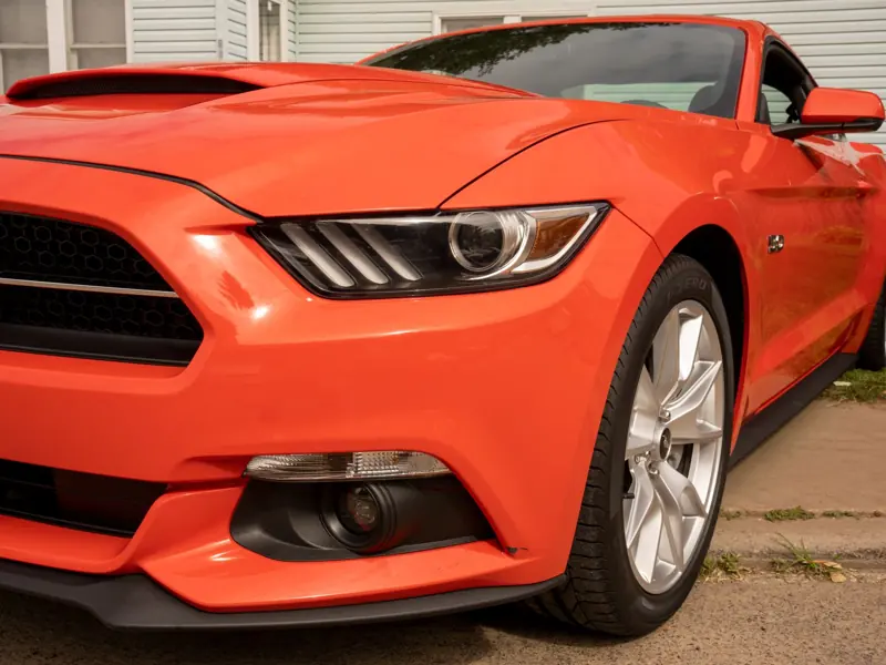 Front view of a bright orange sports car parked on an urban street, showcasing sleek design.