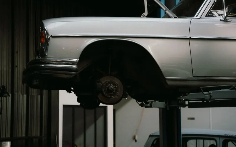 A classic car is elevated on a lift in a professional auto repair garage, showcasing its undercarriage.