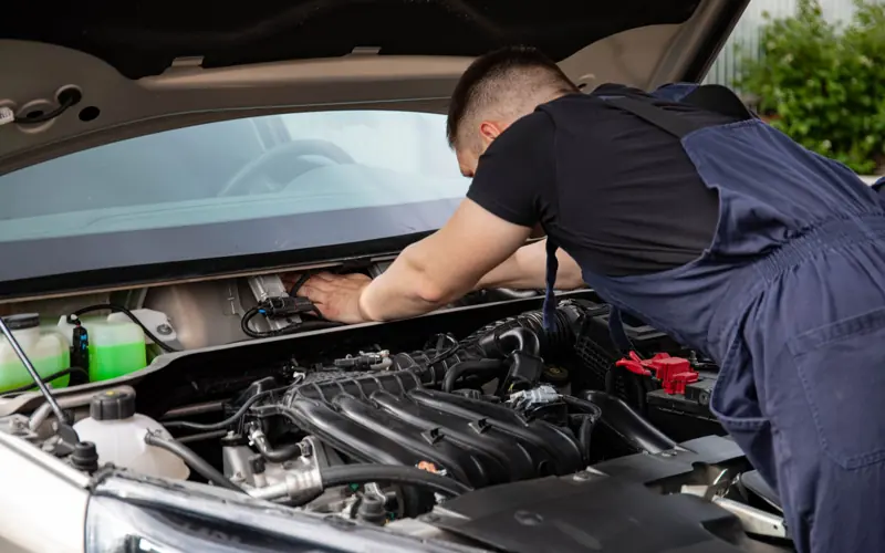 Auto mechanic performs engine maintenance on a car. Focus on hands and engine components.