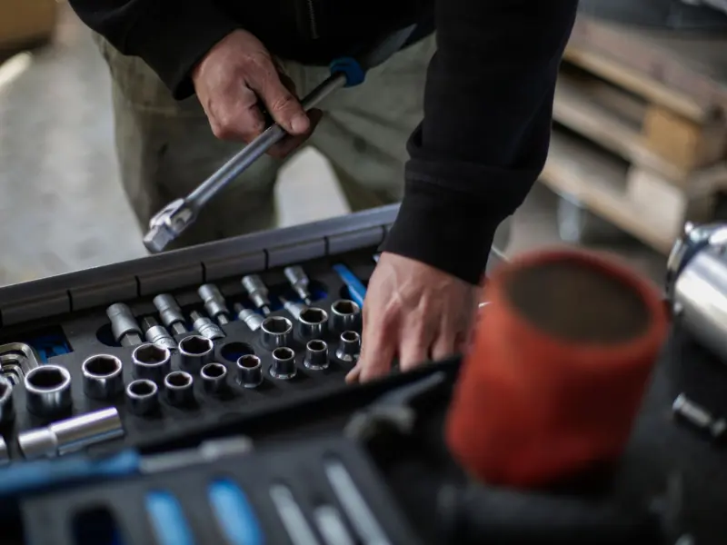 From above view of crop unrecognizable mechanic in workwear choosing metal sockets for ratchet while repairing vehicle in modern workshop