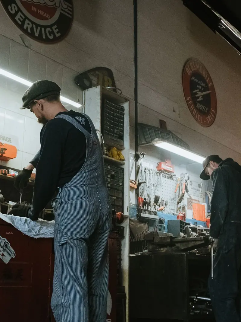 Two mechanics in a garage working on vehicle repair and maintenance.