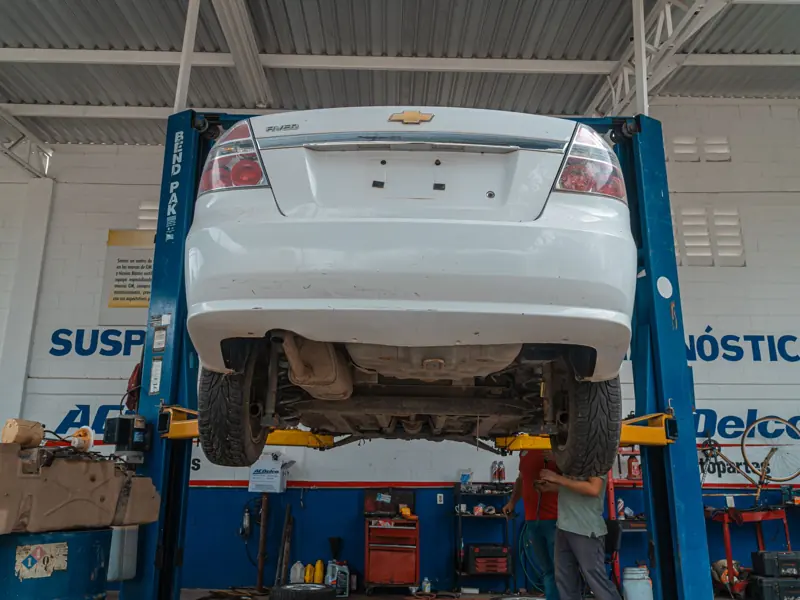 A white Chevrolet car is lifted for maintenance in an automotive repair shop.