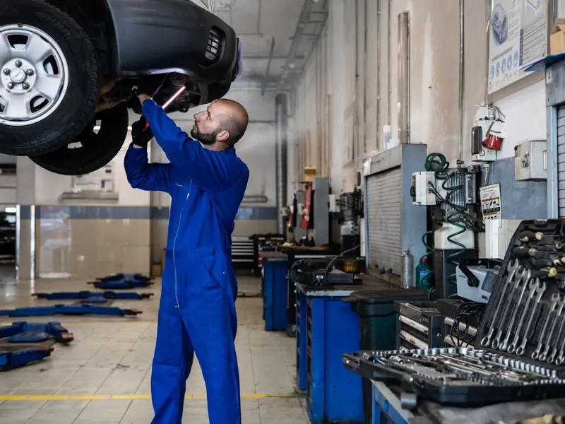 Mechanic inspecting a raised car in an auto workshop for maintenance and repair services.