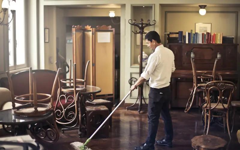Side view of young ethnic male in uniform cleaning floor with mop while working in retro styled restaurant
