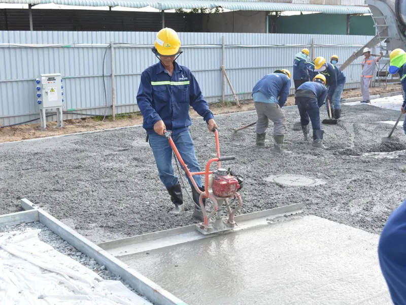 Team of workers smoothing and leveling wet concrete at a construction site.