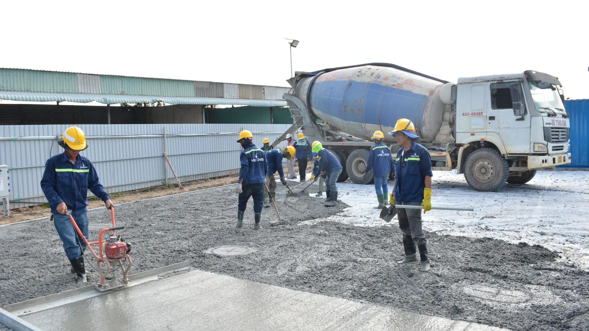 Team of workers pouring cement from a mixer truck on a construction site, ensuring proper leveling.