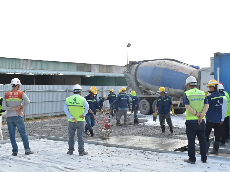 Team of workers in helmets and vests collaborating on a construction site with cement mixer truck.