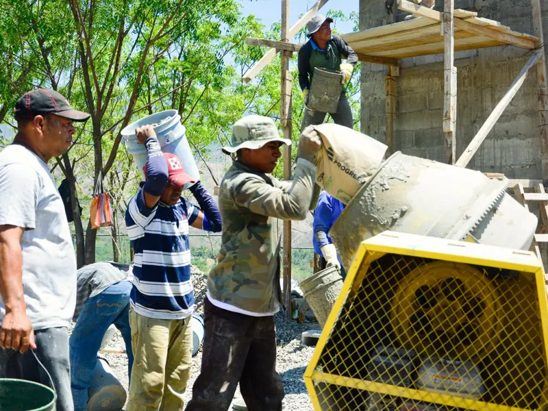 Outdoor construction site with workers pouring cement from mixers and buckets.