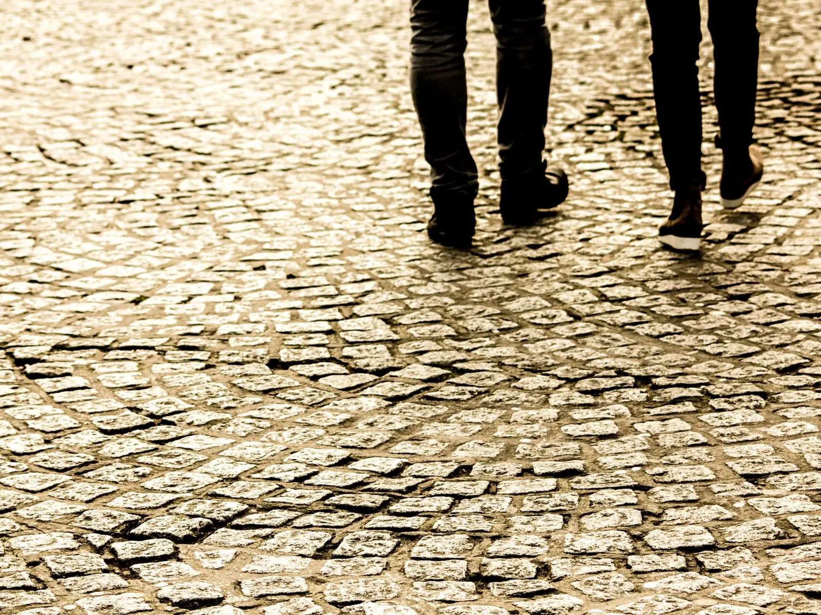 Two people walking on a textured cobblestone street, capturing motion and pattern.