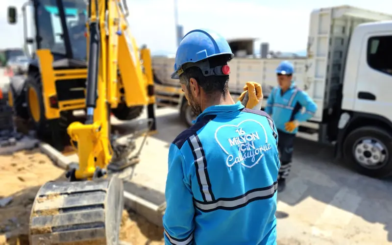 Construction workers operating excavator at a road site, ensuring progress and safety.