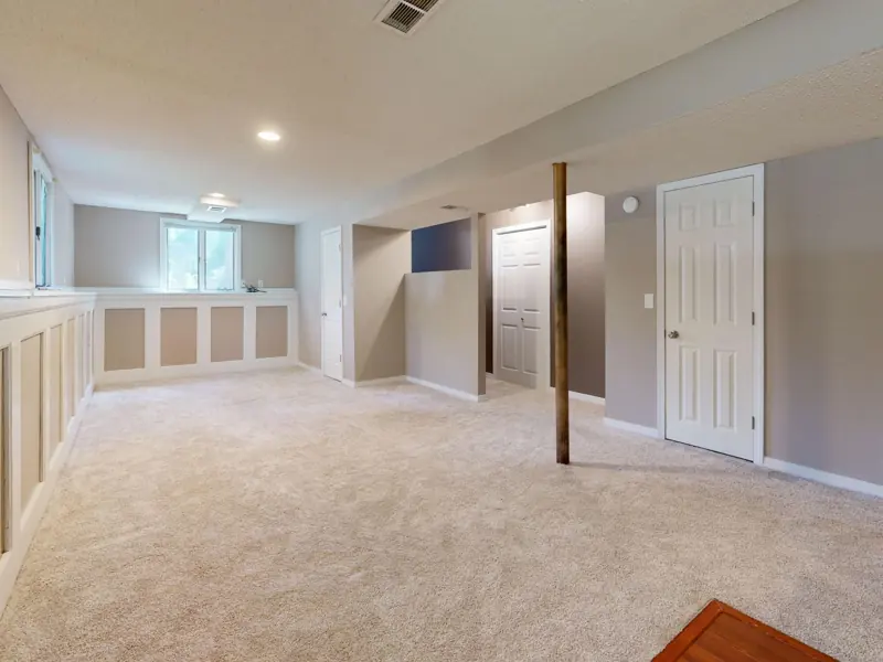 Bright and clean modern basement with carpet flooring and recessed lighting.