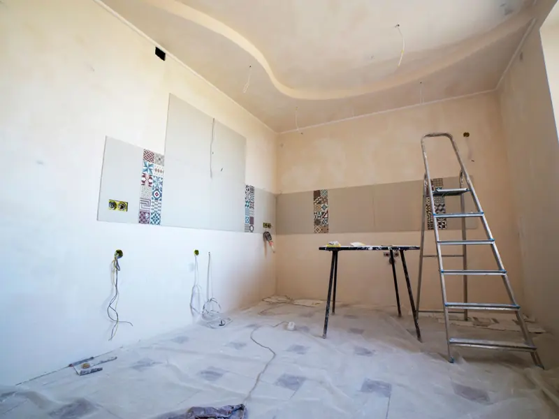 Interior view of a room under renovation with paint, tiles, and tools.