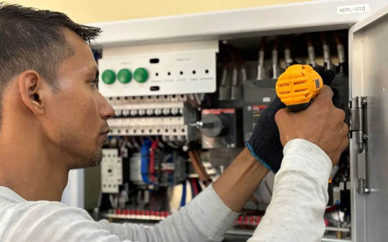 Skilled electrician using a drill to repair electrical equipment indoors. Focus on precision and safety.