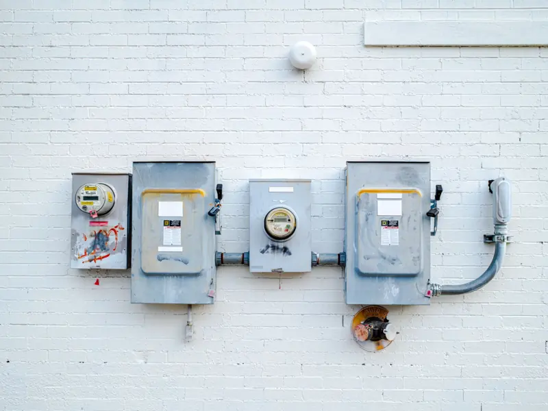 Electrical boxes and power meters mounted on a white brick wall.
