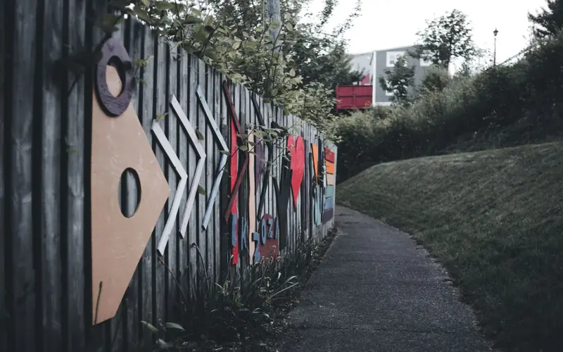 Vibrant geometric and heart designs adorn a wooden fence lining a quiet paved path.