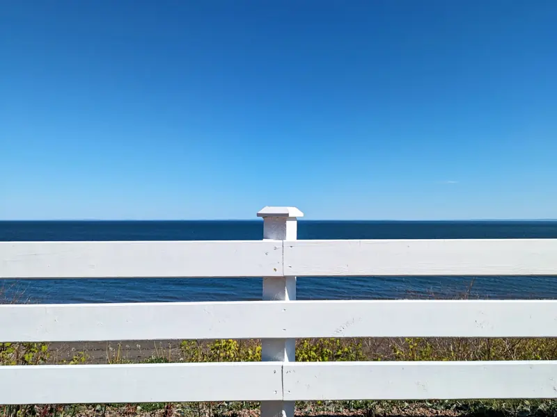 Serene view of a white wooden fence facing the ocean under a clear blue sky in summer.
