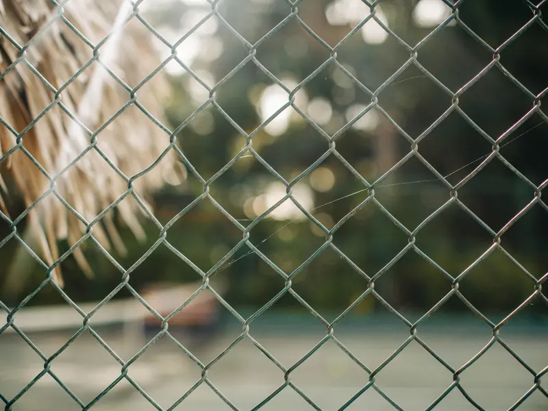Detailed view of a chain link fence against a blurred outdoor backdrop.