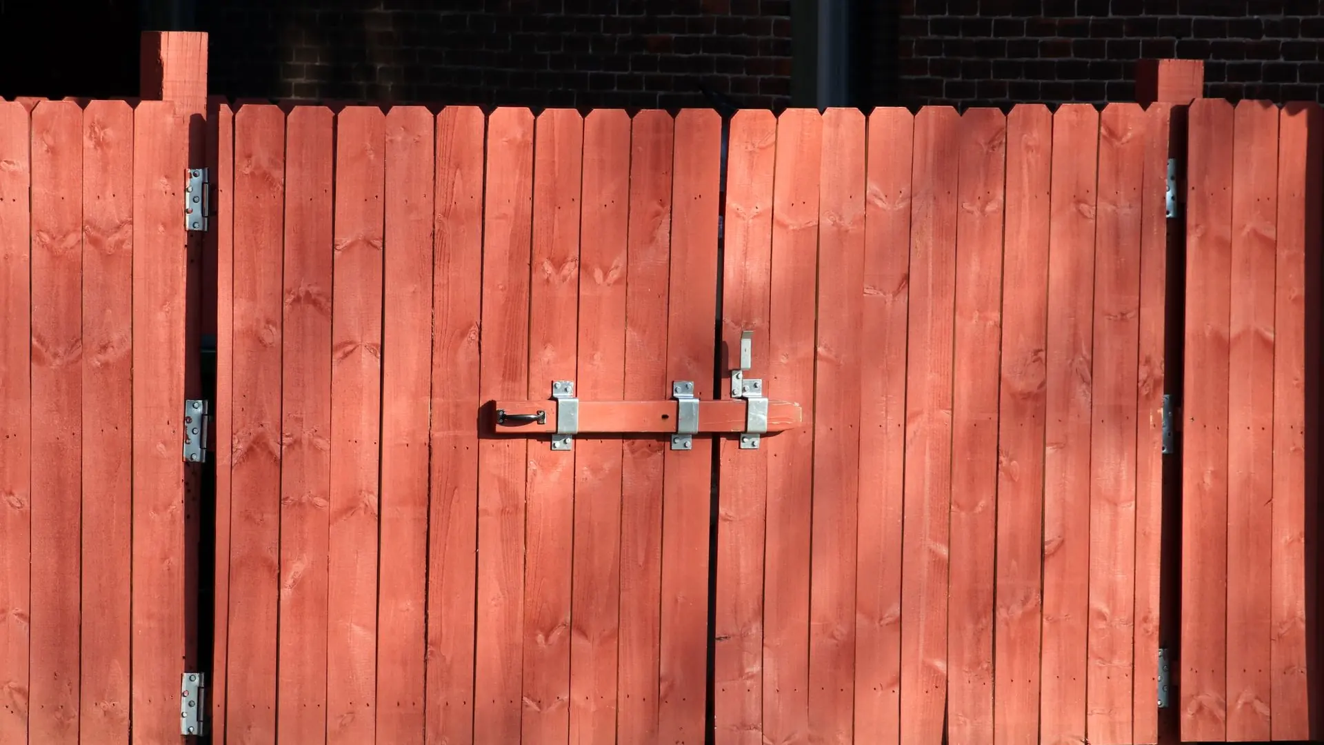 Rustic red wooden fence with a metal latch, ensuring safety and security outdoors.