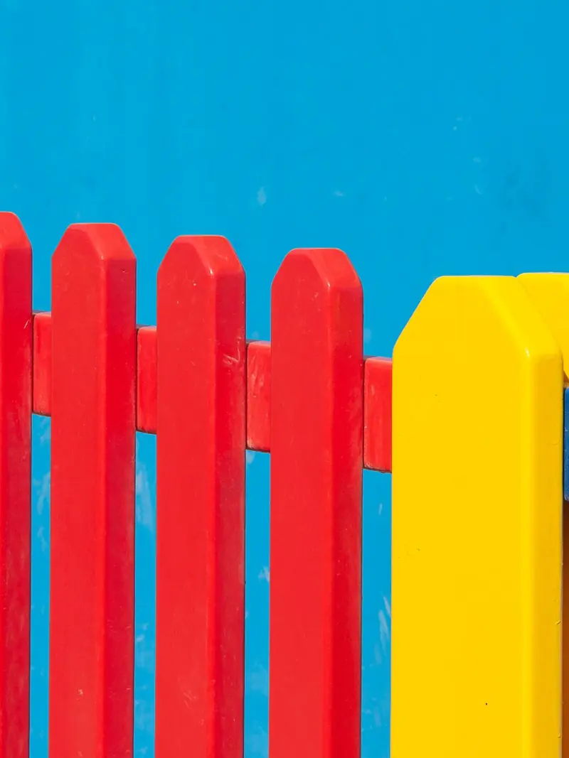 Vibrant red, yellow, and blue wooden fence panels against a clear blue backdrop.