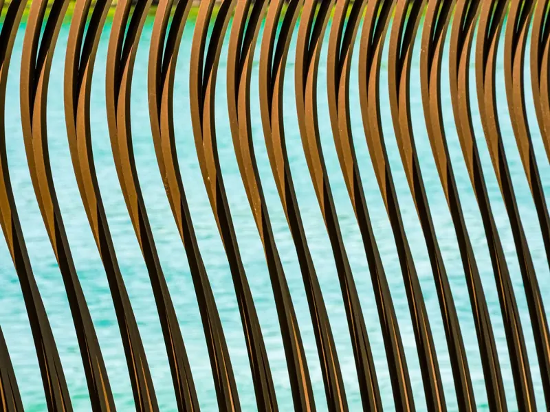 Artistic image of wavy metal bars with a water backdrop, conveying movement.