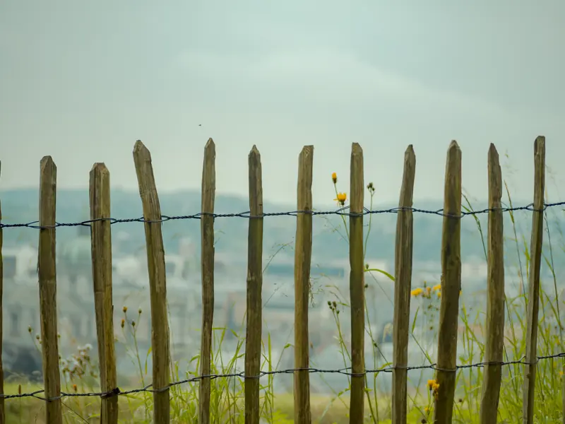 Wooden fence with barbed wire in countryside setting, overlooking scenic landscape.