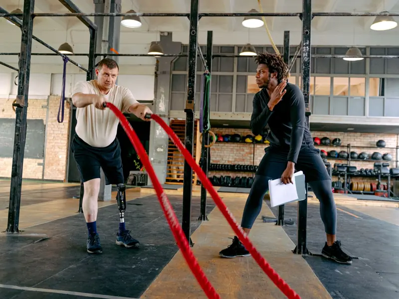 Adaptive training session featuring a prosthetic athlete using battle ropes under professional guidance.