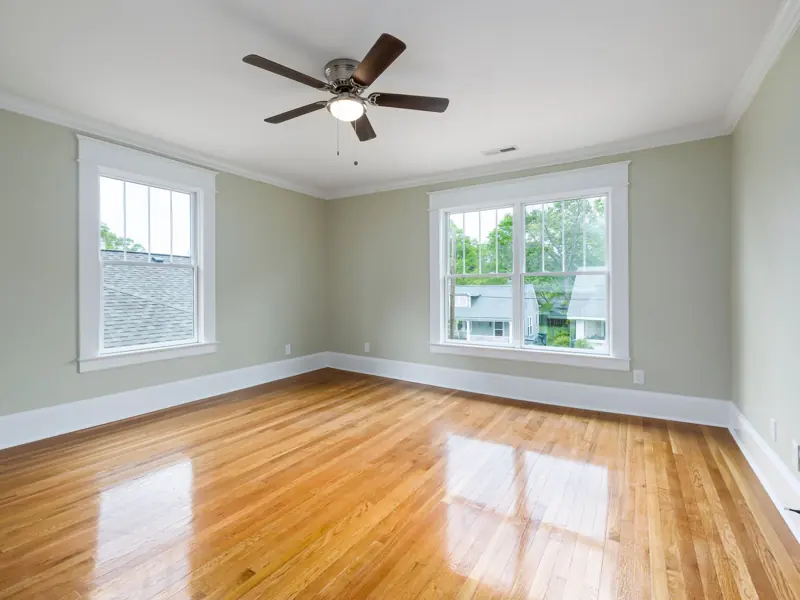 Bright empty room with wooden floors, large windows, and a ceiling fan.