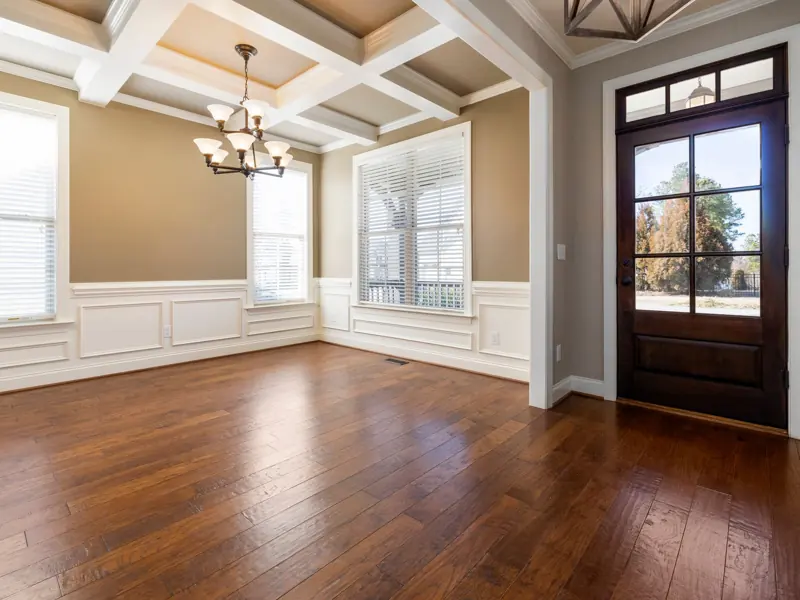 Spacious empty living room with wooden flooring, large windows, and ceiling lights.