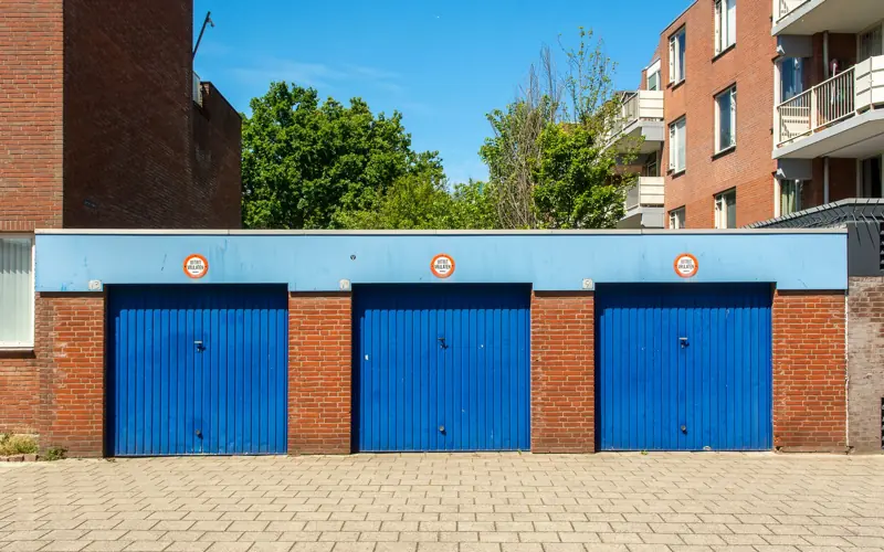 Three blue garage doors in a brick building on a sunny day.