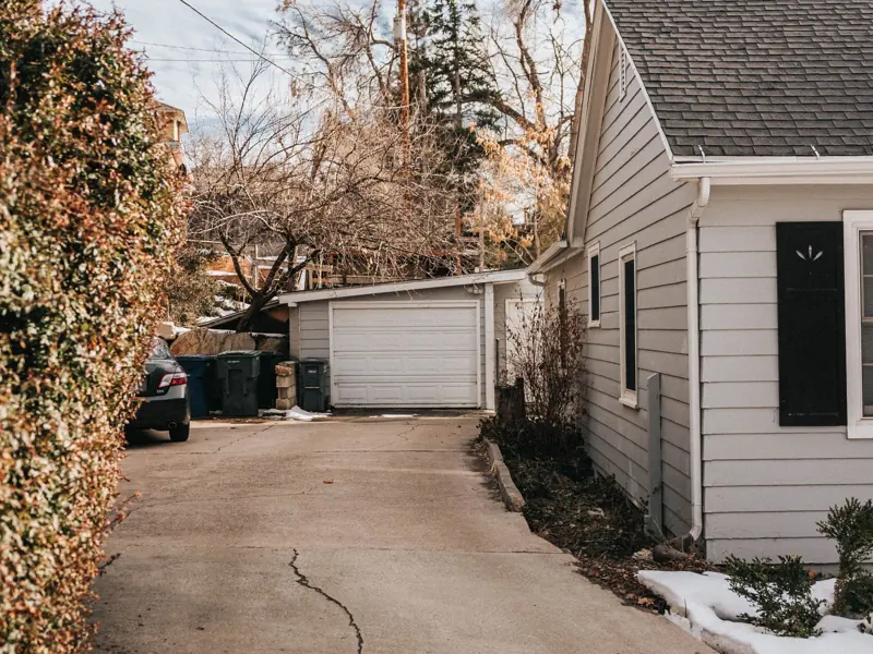 A peaceful suburban driveway with cracked pavement leading to a house surrounded by bare trees.