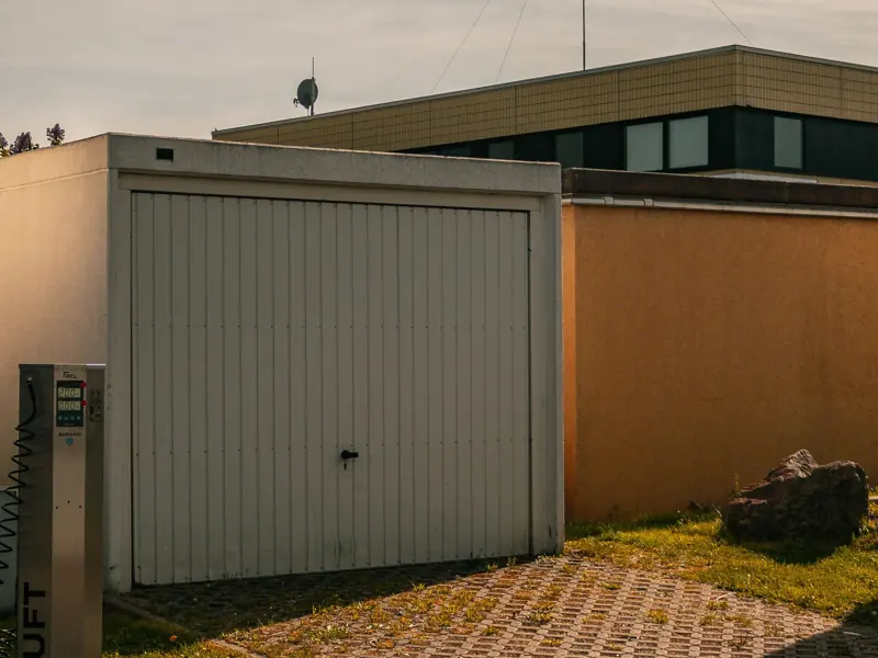 A minimalist urban scene featuring a closed garage, paving stones, and clean lines under a sunny sky.