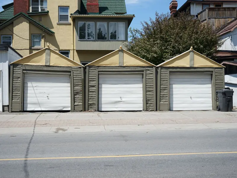 Row of three traditional residential garages with unique roof design on a sunny day.
