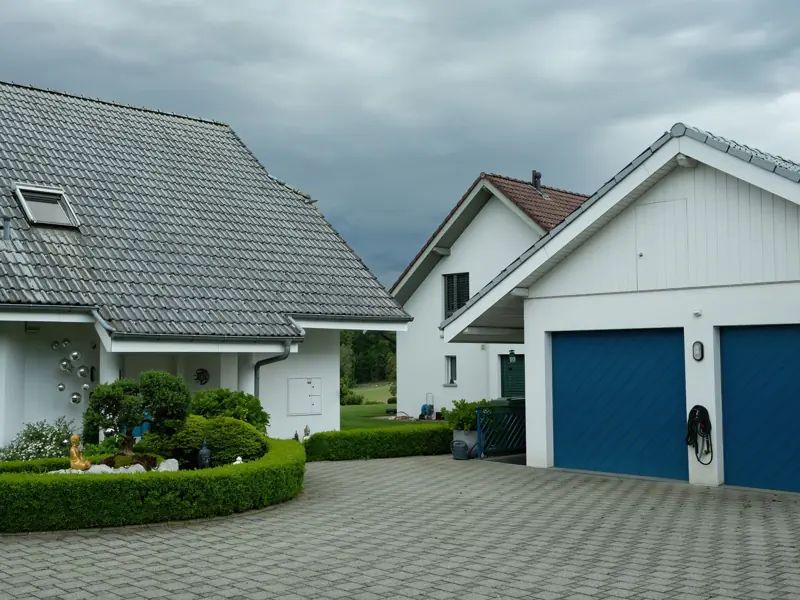 Lovely suburban houses with blue garage doors under cloudy sky, surrounded by greenery.
