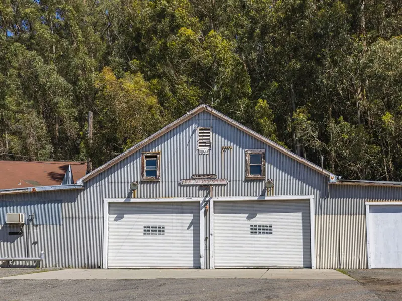 A rustic metal garage with a corrugated facade surrounded by dense trees.
