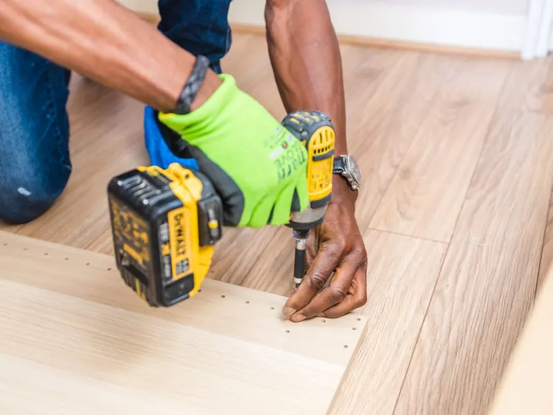 Close-up of handyman drilling wood indoors with green gloves and cordless drill.