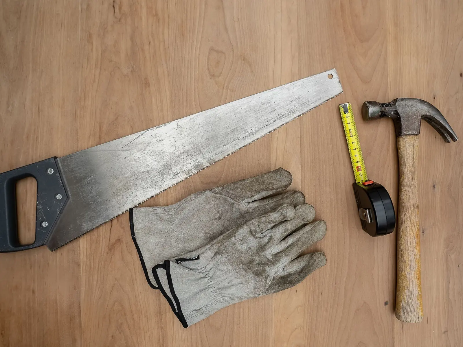 Flat lay of essential carpentry tools including a saw, hammer, and tape measure on wooden surface.