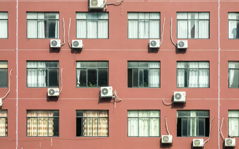 Red building exterior with multiple windows and air conditioners, showcasing urban architecture.