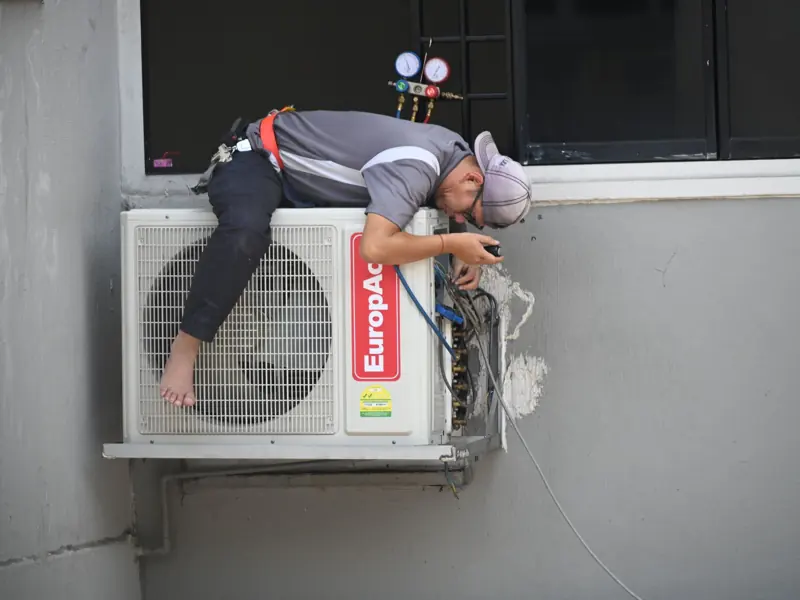A technician skillfully repairing an outdoor air conditioning unit mounted on a building wall.