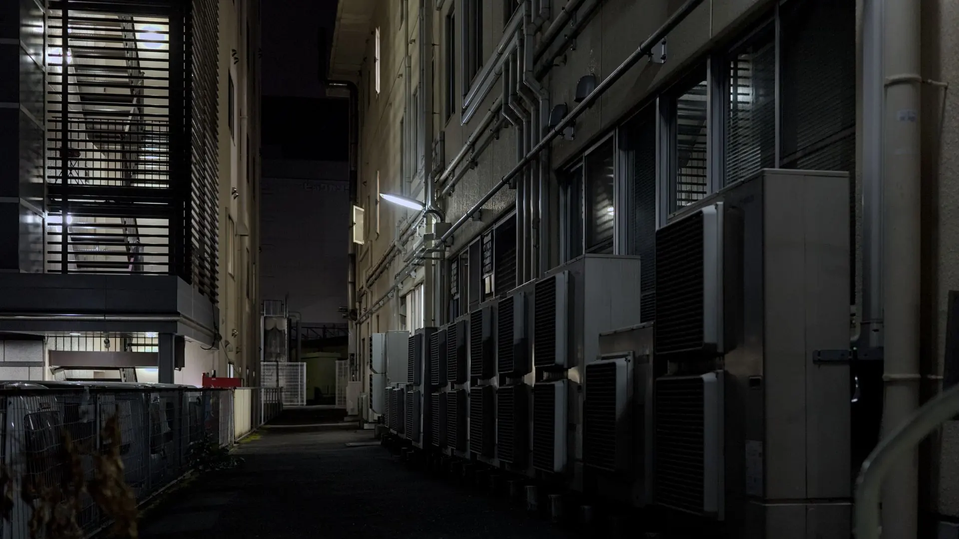 A dimly lit urban alley in Kyoto featuring air conditioning units, captured at night.