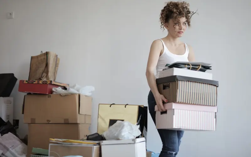 Focused female in casual clothing packaging belongings in boxes for moving in new apartment while standing in messy room and looking away
