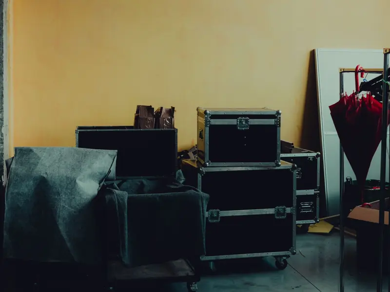 Many boxes and huge iron cases near umbrella placed in room with yellow walls