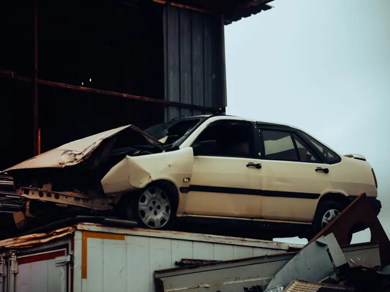 A damaged car sits atop a metal scrap heap, showing a scene of automotive decay.