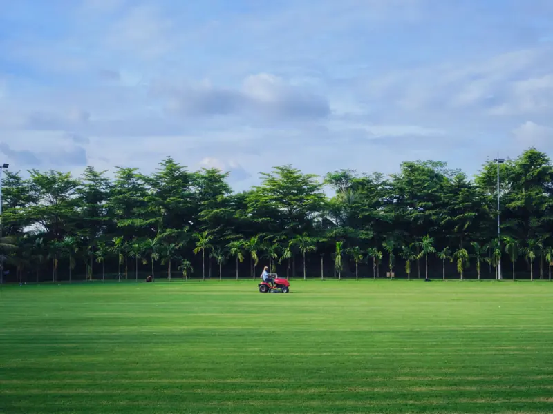 A man mowing the grass on a pristine golf course in Dhaka, Bangladesh, under a clear summer sky.